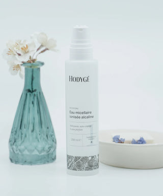 l'eau micellaire Hodygé au centre un pot de fleur bleu à gauche et un porte savon beige à droite