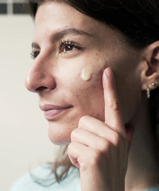 jeune femme en pull bleu applique le soin hydratant Hodygé sur son visage avec le doigt